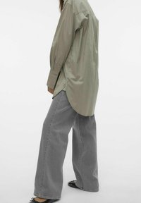 Lichtgroen button-up shirt met lange mouwen, zijsplitten en een gebogen zoom, gecombineerd met losse grijze denim jeans.