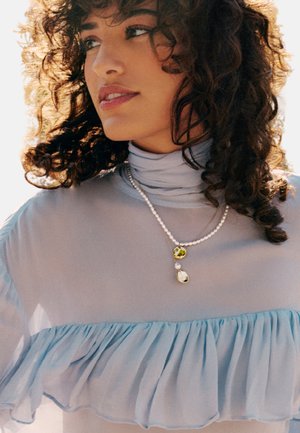 Light blue blouse with ruffle detail, featuring a high collar. Layered pearl necklace with yellow and clear gemstone accents.