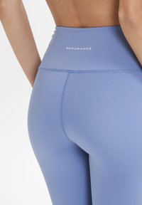 Leggings de sport bleus avec une taille haute, présentant une texture lisse et des coutures visibles, marqués du mot "ENDURANCE" en blanc.