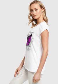 Hvid bomulds t-shirt med korte oprullede ærmer, med et stort lilla sommerfuglegrafik og sort tekst. Casual fit, glat tekstur.