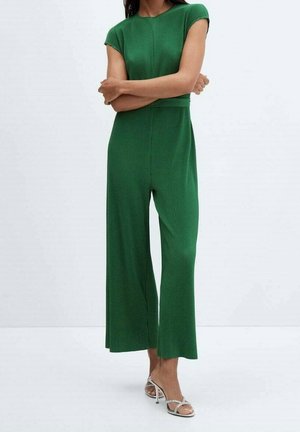 Mono verde acanalado con un torso ajustado, mangas cortas, piernas anchas y una textura suave. Combinado con tacones abiertos plateados.