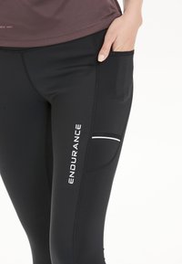 Zwarte sportleggings met een slanke pasvorm, voorzien van een zijvak en witte tekst "ENDURANCE". Gemaakt van rekbaar, vochtafvoerende materiaal.