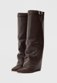 Bottes en cuir marron, montantes, au design structuré et décontracté, avec un bout pointu et une texture lisse. Présentant un accent de boucle en argent en haut.