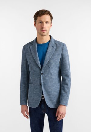 Lyseblå blazer lavet af tekstureret stof, med en notch-revers, to forlommer og enkelt knaplukning, båret over en blå skjorte.