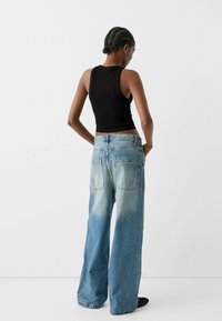 Black fitted tank top paired with wide-leg light blue jeans, featuring a faded wash and two back pockets. Smooth fabric texture throughout.