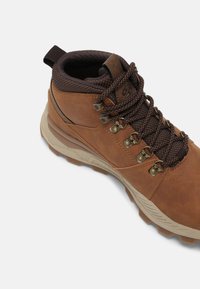 Braune Ledermännerwanderschuhe mit strukturiertem braunem Stoffkragen, Metallbeschlägen und robustem beigem Profilsohle. Verfügt über braune Schnürsenkel und Zugschlaufe.