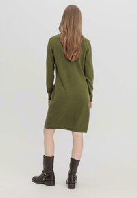 Vestito a maglia verde realizzato in tessuto morbido, con maniche lunghe e silhouette dritta, abbinato a stivali marroni fino al ginocchio.