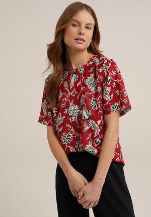 Red floral short-sleeve blouse with black and white flower patterns, round neckline, and a loose fit, paired with black trousers.