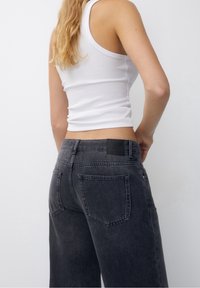 Black denim high-waisted jeans with a loose fit, featuring back pockets and a leather patch on the waistband. Texture appears soft.