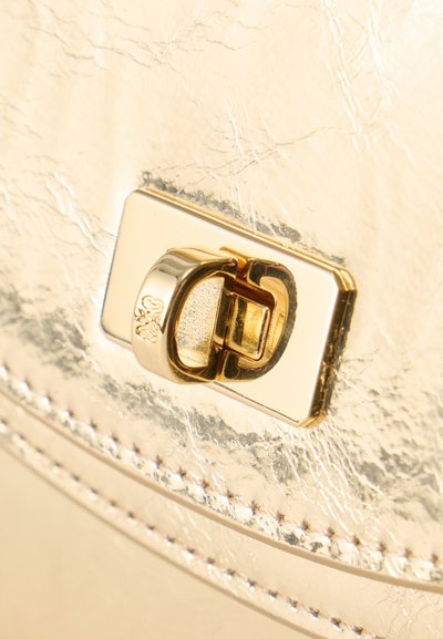 Κοντινό πλάνο μεταλλικού χρυσού κούμπωμα τσάντας με ορθογώνια βάση και μηχανισμό κλειδώματος με περιστρεφόμενο βρόχο.