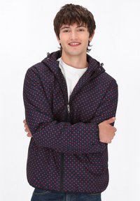 Giacca trapuntata blu navy con pois rossi, dotata di chiusura con zip e cappuccio regolabile. Texture liscia, design casual e maniche lunghe.