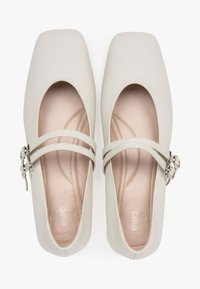 Beżowe buty na kwadratowym nosku z podwójnymi krzyżującymi się paskami i srebrną klamrą. Wykonane z miękkiej skóry, posiadają gładką teksturę wewnątrz.