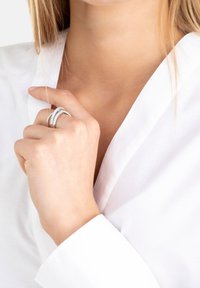 Tre silverringar staplade tillsammans, med en slät band, en pärlstruktur och en rad av små ädelstenar, bärs på en hand mot en vit skjorta.