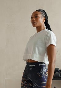Hvid cropped atletisk t-shirt med korteærmer og en subtil linjedetalje. High-waisted leggings med et mørkt mønster og farverige accenter.