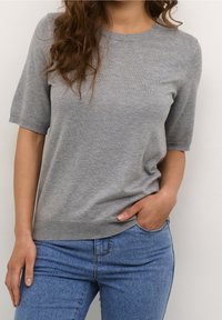 Šedý pletený svetr s krátkými rukávy, kulatým výstřihem a volným střihem. V kombinaci s světle modrými džínami. Hladká textura, minimalistický design.
