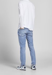 Ljusblå denimjeans med avslappnad passform, som har två bakfickor och subtila sömdetaljer, kombinerat med en vit långärmad skjorta och sneakers.