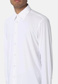 Camicia bianca a maniche lunghe realizzata in tessuto liscio, con colletto a punta, apertura frontale con bottoni e vestibilità su misura. Nessun motivo o dettaglio visibile.
