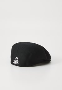 Black textile beret with a smooth texture, rounded shape, and a small white logo on the side. Suitable for casual wear.