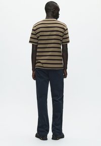 Stribet kortærmet t-shirt i brun og beige, parret med mørkeblå bukser. Stoffet ser blødt ud; pasformen er afslappet og uformel.