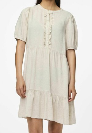 Robe beige à manches courtes avec patte de boutonnage à volants, manches bouffantes et ourlet à étages portée par une personne debout sur un fond blanc.