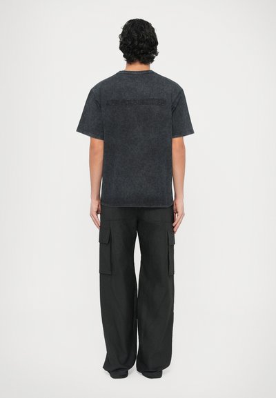Črna denim majica s rahlo teksturirano površino in sproščenim krojem, kombinirana z širokimi črnimi cargo hlačami s stranskimi žepi.