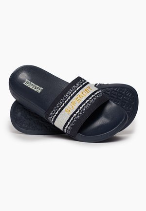 Mørkeblå slidesandaler med en tekstureret sål. Med en bred stofrem i sort og elfenben med "SUPERDRY" broderet i guld.