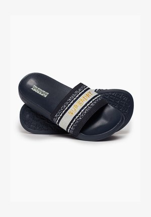 Navyblauwe instapsandalen met een gestructureerde zool. Voorzien van een brede stoffen strap in zwart en ivoor met "SUPERDRY" geborduurd in goud.