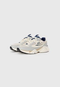 Ett par beige och grå FILA-sneakers med marinblå detaljer och kraftiga vita sulor mot en enkel vit bakgrund.