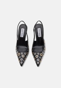 Chaussures à talons slingback noires à bout pointu, dotées d'œillets métalliques en or et en argent, avec une finition en cuir lisse et un design à talon ouvert.