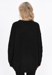 Czarny, oversize sweter o teksturowanym wykończeniu, z haftowanymi wzorami na rękawach i okrągłym dekoltem. Miękki, przytulny materiał.