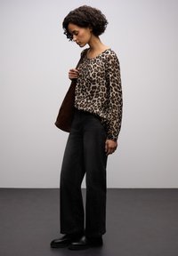 Bluzka z długim rękawem w panterkę zestawiona z czarnymi, wysokim stanem jeansami i czarnymi botkami za kostkę. Strój charakteryzuje się luźnym krojem i subtelnymi teksturami.