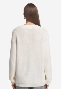 Vit stickad tröja med lös passform, breda ärmar och en texturerad mönstring. Har en rundad halsringning samt ribbade muddar och fåll.