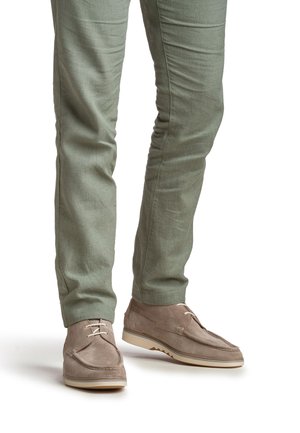 Chaussures en daim beige avec lacets et semelles en caoutchouc blanc, assorties à un pantalon ajusté vert clair, présentant une texture lisse et une coupe sur mesure.