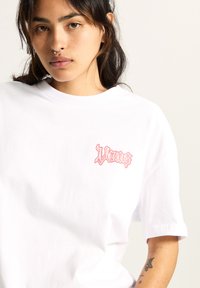 Hvid bomulds t-shirt med et pink grafisk logo på venstre bryst. Klassisk rund hals med korte ærmer og afslappet pasform.