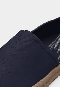 Παπούτσι χωρίς κορδόνια από καμβά σε ναυτικό μπλε με ελαστική γλώσσα σε σχήμα V, ριγέ εσωτερική επένδυση και λεπτομέρεια στην άκρη της σόλας από μπεζ πλεκτό υλικό.