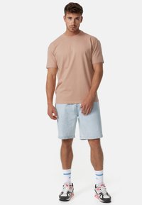 Camiseta de algodón rosa claro combinada con pantalones cortos de mezclilla azul claro. El modelo lleva calcetines blancos con rayas azules y zapatillas negras con acentos rojos.