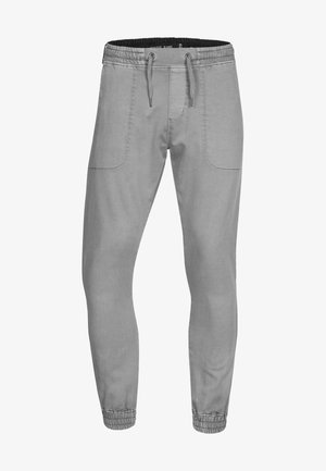 Szare dresowe spodnie z elastycznym pasem, sznurkiem i ściągaczami przy kostkach; mają boczne kieszenie i gładki, teksturowany materiał.