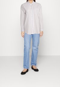 Lightly striped, long-sleeve button-up shirt in beige and white, paired with blue jeans and black flats. The shirt features a chest pocket.