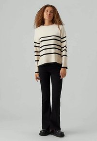 Crème gebreide trui met zwarte horizontale strepen, ronde halslijn en lange mouwen. Gekocht met zwarte flared broek en zwarte platte schoenen.
