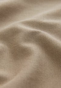 Tejido texturizado en un cálido beige con un patrón de tejido visible y suaves caídas, creando una apariencia lisa y ondulada.