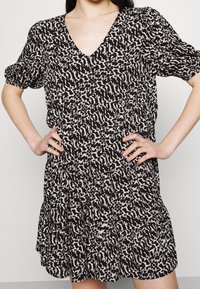 Robe à motifs noirs et crème avec un col en V, des manches courtes bouffantes et une jupe à volants. Confectionnée dans un tissu léger, coupe décontractée.