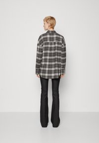 Camicia di flanella a scacchi bianco e nero con vestibilità comoda, colletto a camicia e maniche lunghe; abbinata a pantaloni neri a zampa d'elefante.