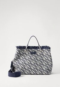 Grand sac fourre-tout en tissu tissé avec un motif en zigzag bleu marine et blanc, bord supérieur à franges, double poignées et bandoulière amovible.