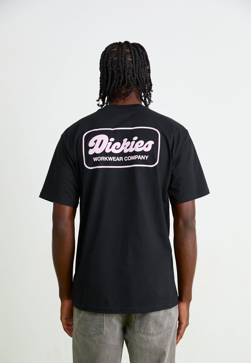 Black cotton T-shirt featuring a pink graphic on the back with the text "Dickies WORKWEAR COMPANY." Short sleeves and relaxed fit.