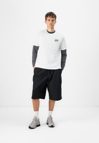 White T-shirt layered over gray long-sleeve shirt, paired with black shorts. Gray sneakers. Clean design, casual fit, minimal detailing.