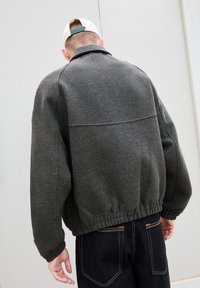 Giacca in pile grigia con colletto, polsini e vita elastici. Il retro presenta un design semplice con cuciture minime e una finitura testurizzata.