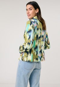 Multicolored blazer with abstract pattern featuring green, blue, and pink hues. Long sleeves, tailored fit, and smooth fabric texture.