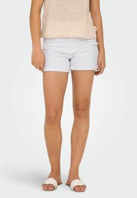 Shorts di jeans azzurri con risvolti. Il materiale sembra morbido con una texture liscia. Abbinati a sandali piatti intrecciati di colore bianco.