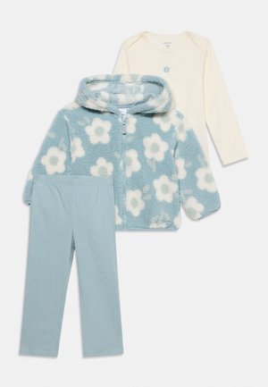 Ensemble bébé trois pièces composé d’un haut crème à manches longues, d’une veste polaire bleue à imprimé floral et d’un pantalon bleu assorti.