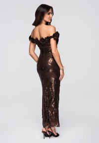 Robe marron à sequins décolletée épaules avec ornements floraux au niveau du col, coupe ajustée, et fentes pour faciliter le mouvement. Talons aiguilles visibles.